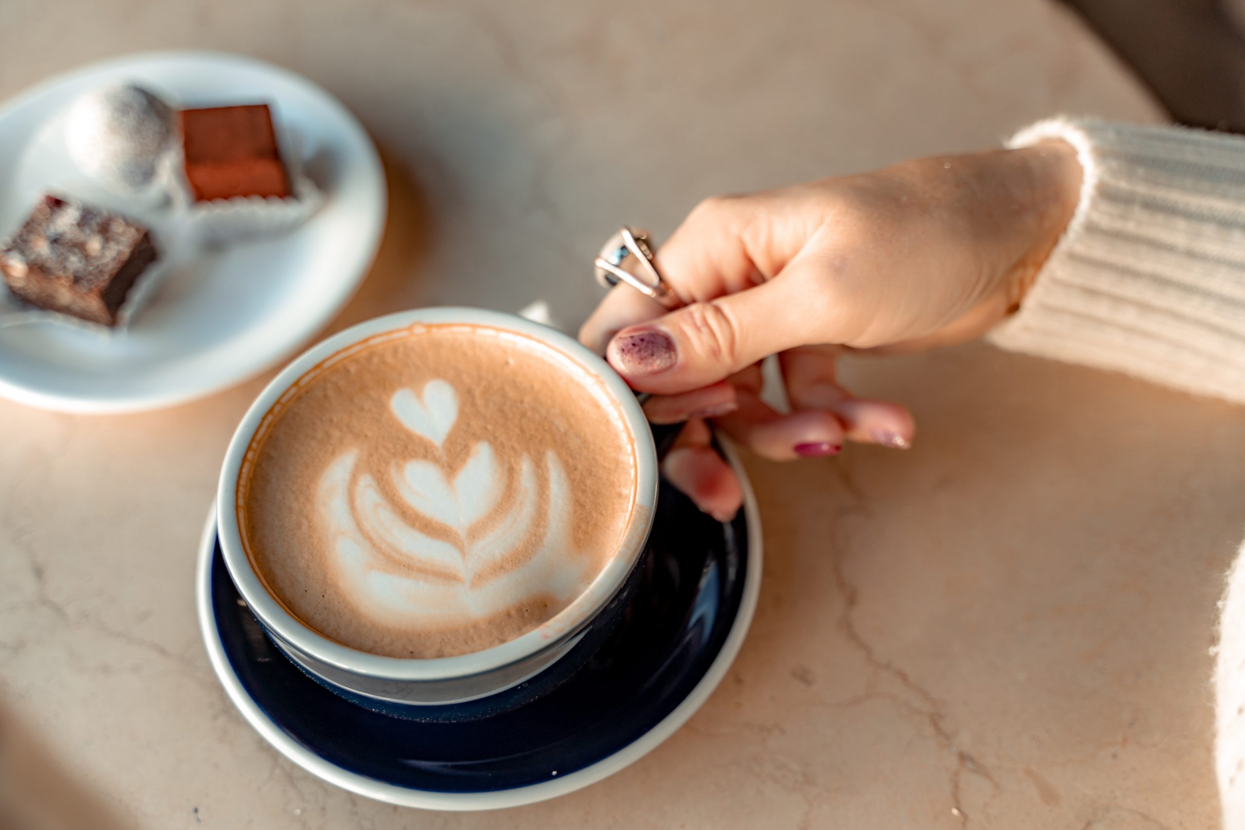 A Cup Of Fresh Cappuccino Coffee In The Hands Of A Woman On A Fa