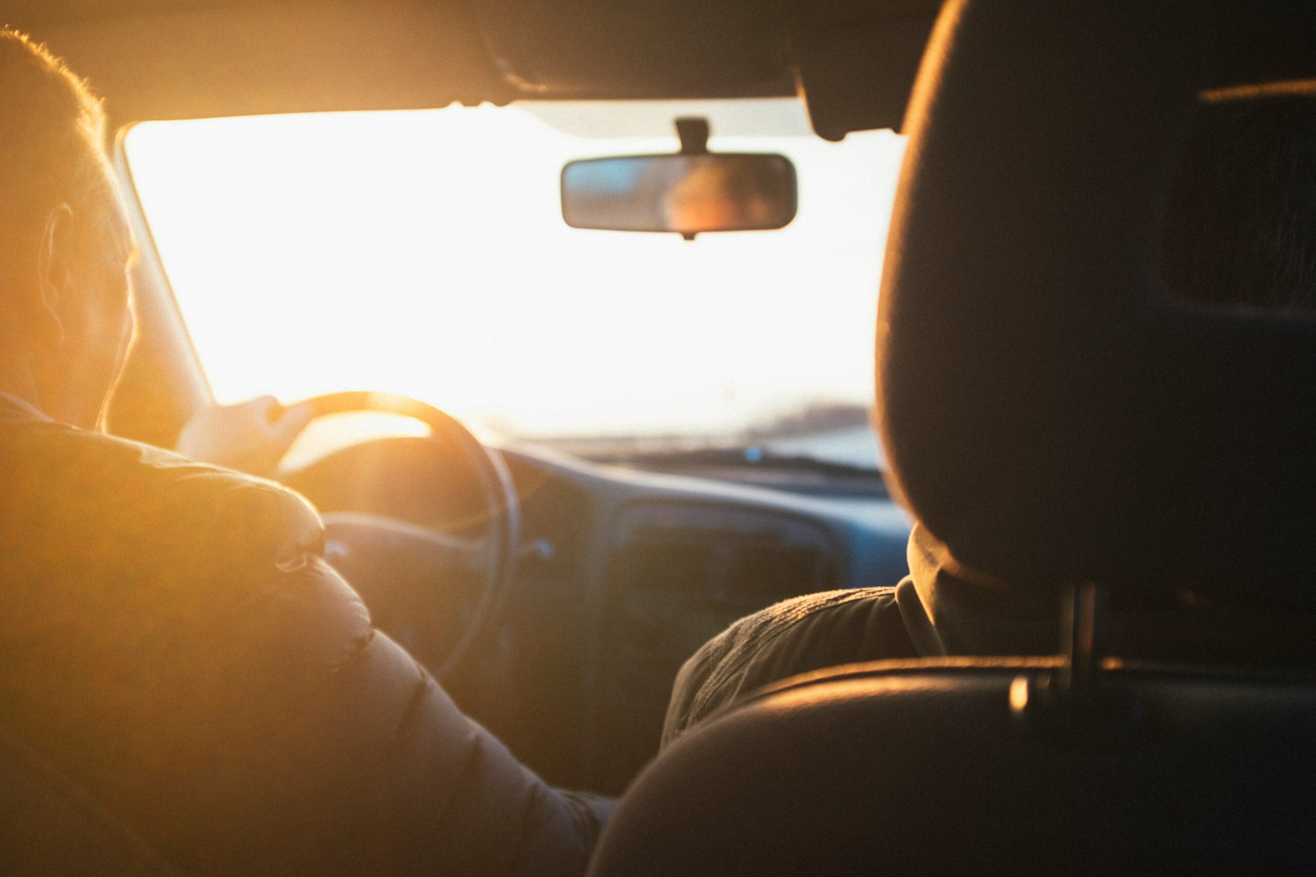 Couple driving into the sunset, view from the back seat