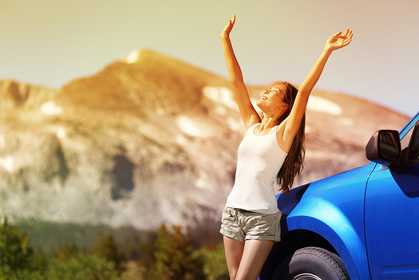 Happy woman standing next to her rental car on a road trip